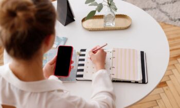 Overhead view of a woman using a smartphone and writing in a notebook at a desk for blog post top-rated gig apps