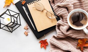 A business woman's home office desk, with a scarf, candle, notebooks, and fall leaves for blog post fall business ideas
