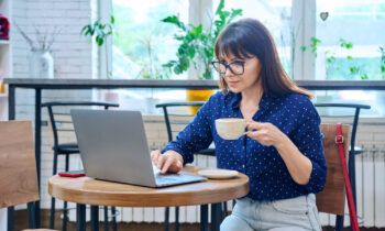 A middle aged woman drinking coffee and reading an article on her laptop titled top careers for people over 50
