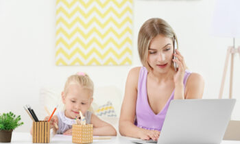A mom and her school aged daughter sitting at the kitchen table with the mom reading an article on how to reenter the workforce