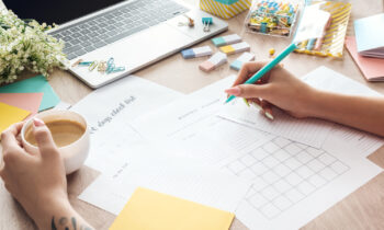 A woman drinking coffee planning her month with printable download sheets