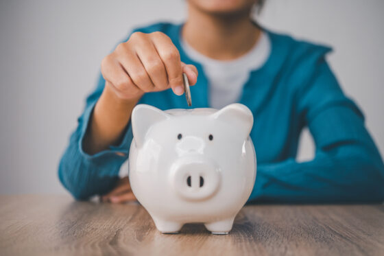A woman putting a coin into a piggy bank for the blog post how to earn $100 a day