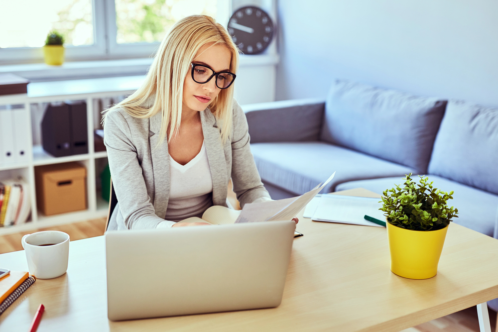 A woman with long hair and glasses reading an article on real work from home jobs