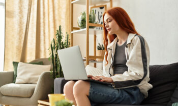 A woman with red hair sitting on her sofa looking for remote facebook jobs on her laptop