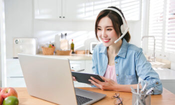 A young female working on her laptop in her kitchen reading an article about TTEC jobs you can do from home