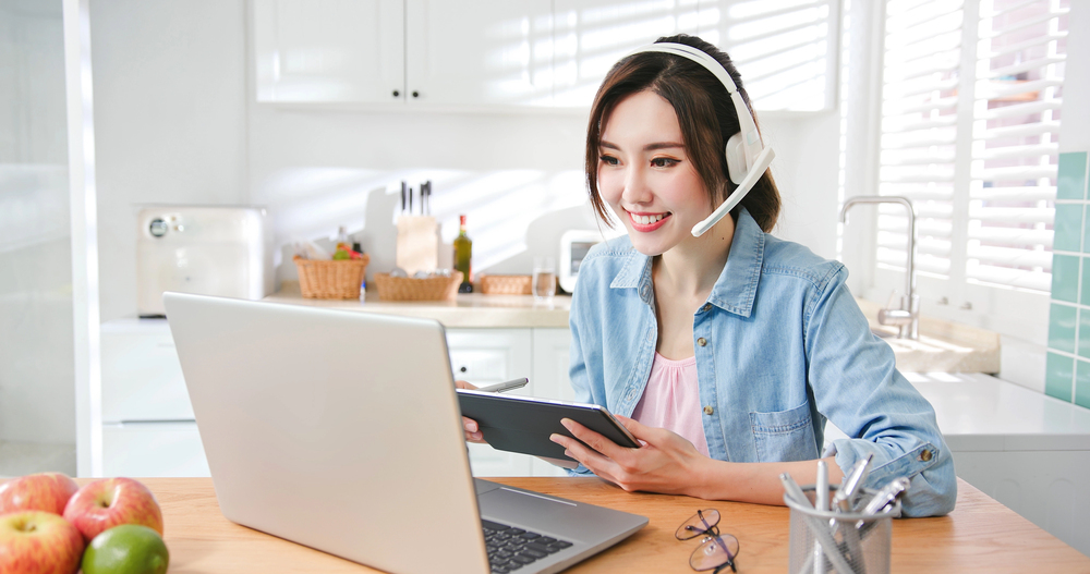A young female working on her laptop in her kitchen reading an article about TTEC jobs you can do from home