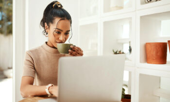 A young woman drinking coffee and reading a FlexJobs review on her laptop