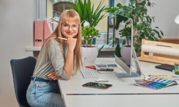 A young woman with long hair and glasses sitting at her desk getting to read an article titled best work at home jobs with Google