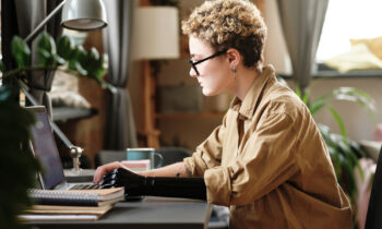 A young woman with short hair, glasses, and prosthetic arm working on her laptop reading an article titled side business ideas