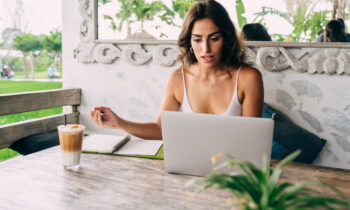 A young woman working at an outdoor cafe reading an article online titled how to make extra money online
