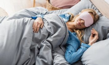 A woman sleeping in bed and wearing a sleep mask for blog post get paid to sleep.