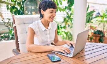 Woman sitting outside on patio working on her laptop looking for legitmate work from home jobs with no startup fees