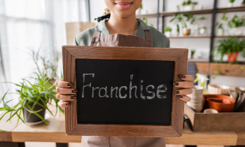 Young woman holding a chalkboard with the word franchise on it for low-cost franchises blog post