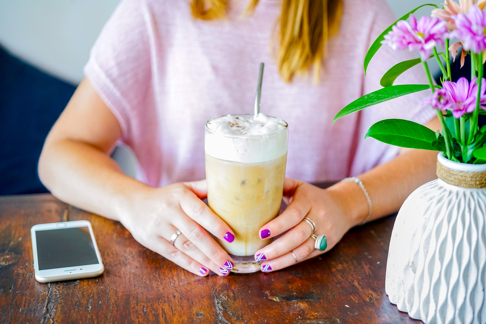 Young woman with painted finger nails drinking an iced coffee in a coffee shop for blog post free starbucks gift cards